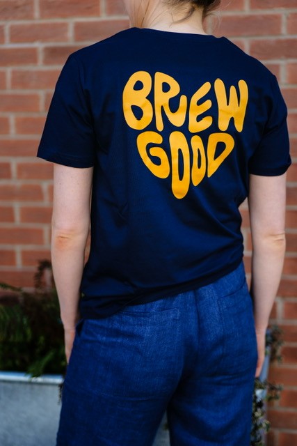 A person wearing a Ritual Coffee navy t-shirt with 'BREW GOOD' text in orange on the back, standing against a brick wall.