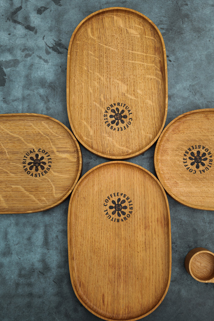 A set of four handcrafted oak trays with the Ritual Coffee logo embossed in the center, displayed on a textured background.