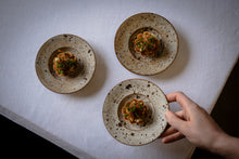 Load image into Gallery viewer, Three ceramic plates with food on a textured white surface, one plate held by a hand.