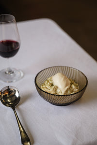 Bowl of dessert with ice cream and a glass of red wine on a white tablecloth.