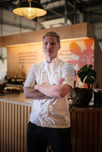Load image into Gallery viewer, Kian Puerto Terron in a white chef&#39;s coat standing infront of the Ritual Coffee cafe with a blurred background
